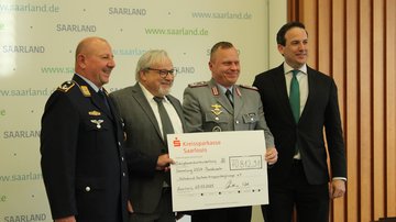 Zwei uniformierte Bundeswehrsoldaten und zwei Herren im Anzug halten einen Scheck in die Höhe