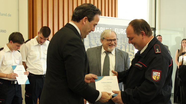 Ein Herr im Anzug überreicht einem Feuerwehrmann eine Urkunde