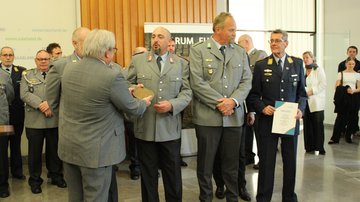 Drei uniformierte Reservisten erhalten eine eiserne Plakette von einem Herrn im Anzug