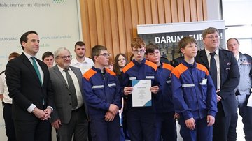 Jugendliche im Feuerwehranzug mit einer Urkunde, rechts und links zwei Herren im Anzug